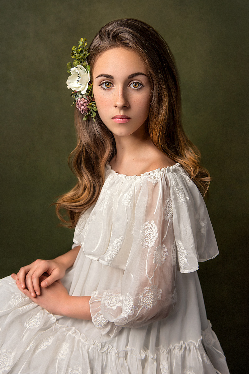 A fine art portrait capturing the beauty of a girl in a white dress adorned with a flower in her hair, crafted by Houston child photographer Tatyana Sokolova