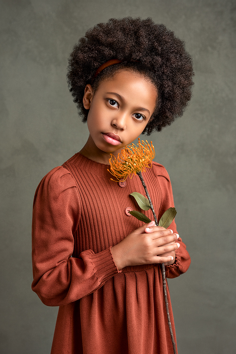 A fine art portrait featuring a gorgeous African American girl in a vintage knitted dress, gracefully holding a flower, captured by Houston child photographer Tatyana Sokolova
